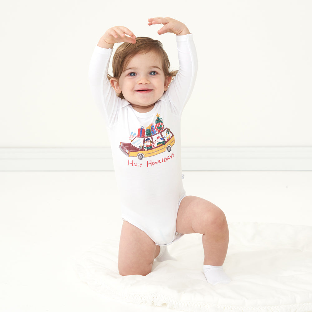 Child kneeling on the ground wearing a Happy Howlidays graphic bodysuit