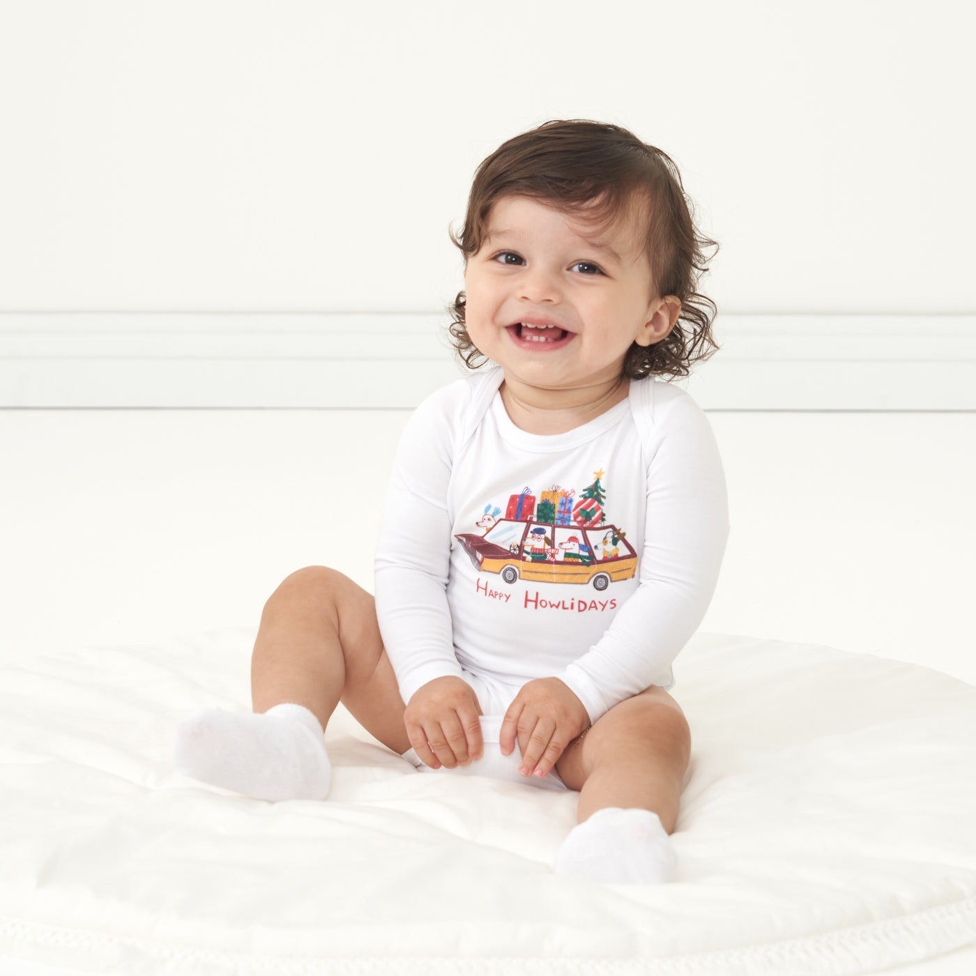 Child sitting on the ground wearing a Happy Howlidays graphic bodysuit