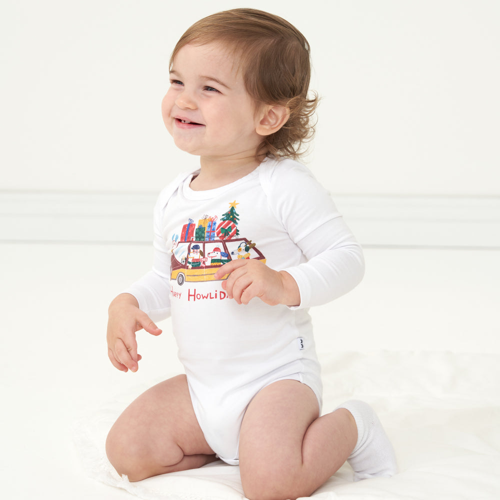 Child kneeling and looking to the side wearing a Happy Howlidays graphic bodysuit