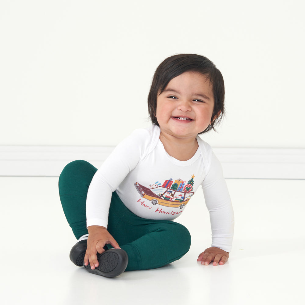 Child sitting on the ground wearing a Happy Howlidays graphic bodysuit and coordinating Emerald joggers