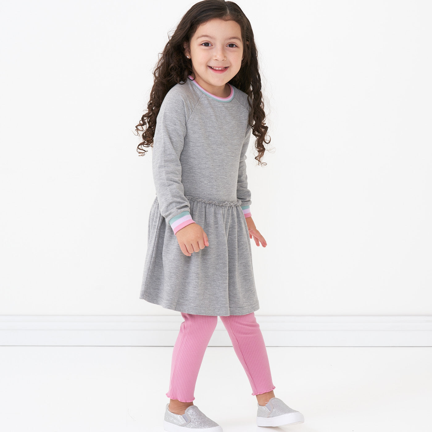 Child posing wearing a Heather Gray drop waist dress paired with Garden Rose ribbed lettuce leggings