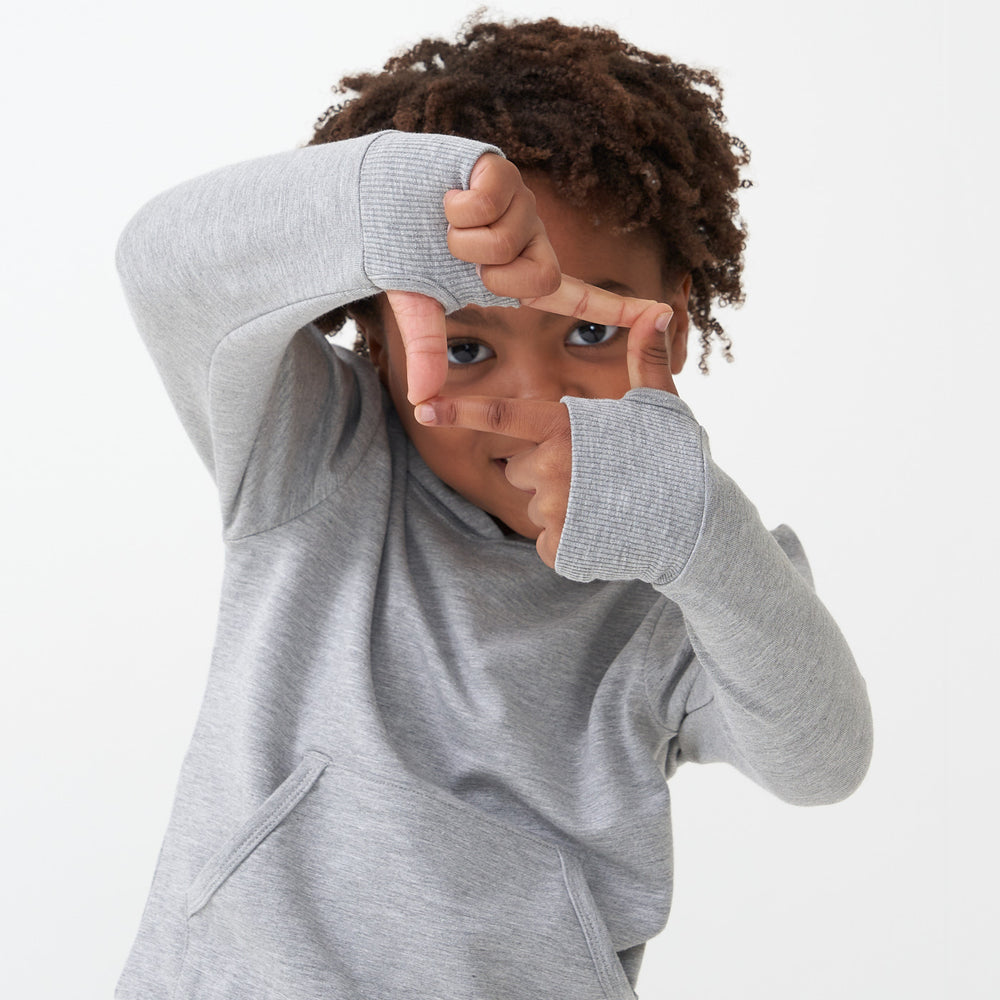 Child posing wearing a Heather Gray pullover hoodie showing off the thumbholes