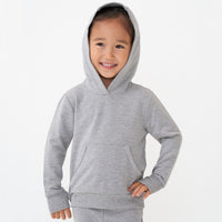 Child posing wearing a Heather Gray pullover hoodie with the hood on her head