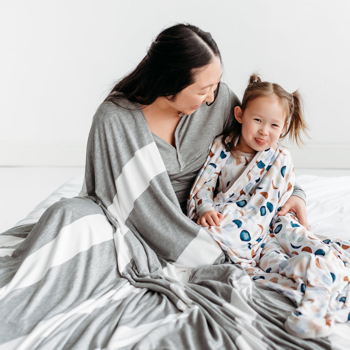 Mother and child sitting on the floor cuddling under a Heather Gray Wide Stripe oversized bamboo blanket and Luna Neutral large bamboo blanket