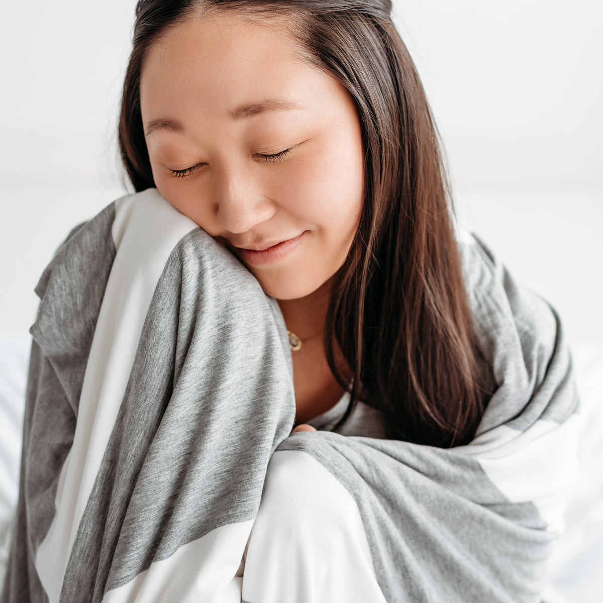 Close up of a woman wrapped up in a Heather Gray Wide Stripe oversized bamboo blanket.