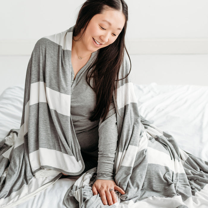 Woman sitting on the ground, wrapped up in a Heather Gray Stripe oversized bamboo blanket