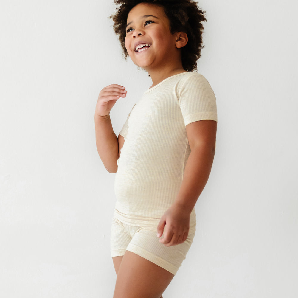 Child posing wearing Heather Oatmeal Ribbed two piece short sleeve and shorts pajama set