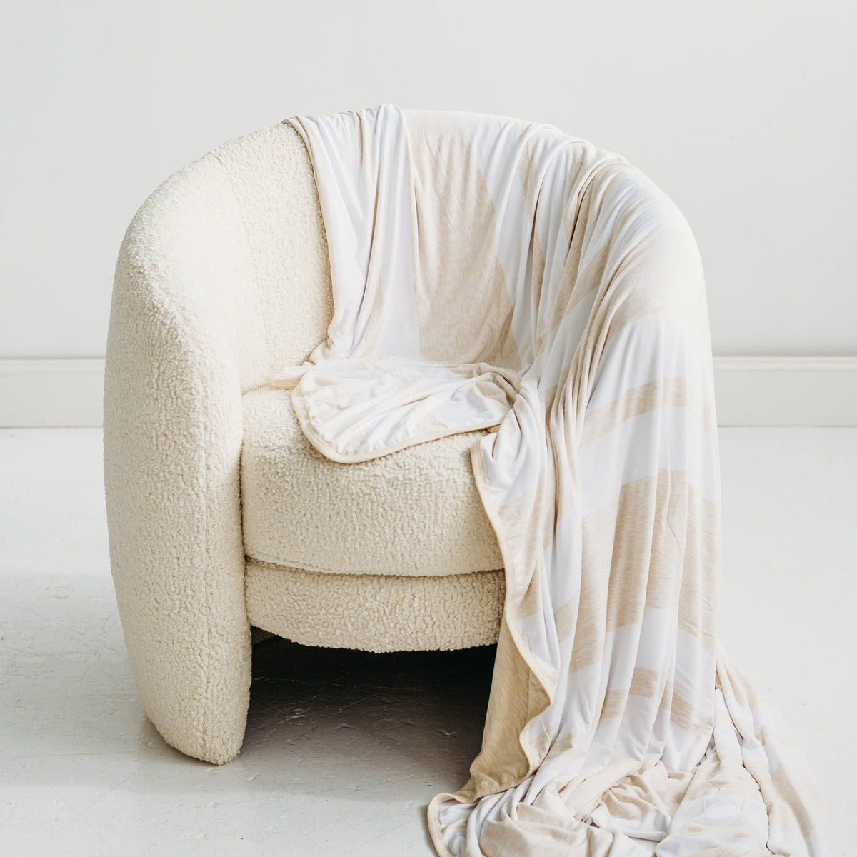 Heather Oatmeal Stripe oversized bamboo blanket draped over the side of a white chair