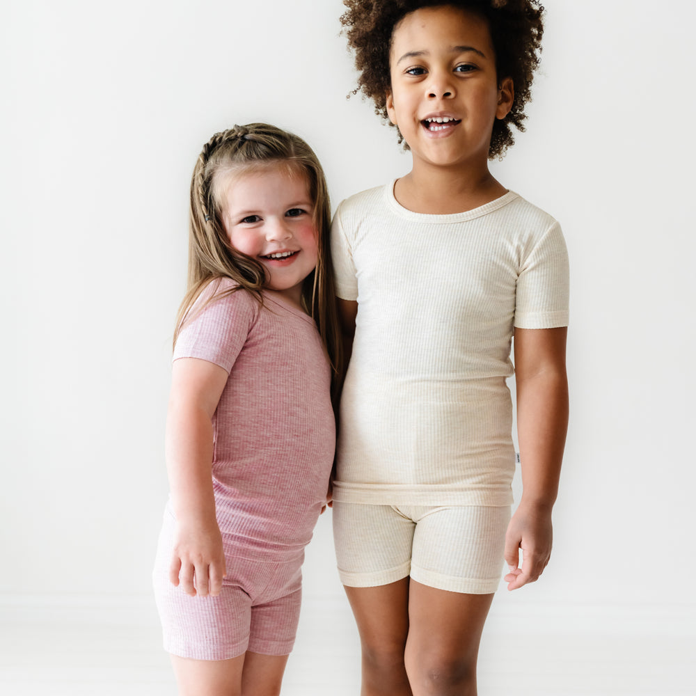 Click to see full screen - Two children posing together wearing Heather Ribbed two piece short sleeve and shorts pajama sets in Heather Mauve and Heather Oatmeal