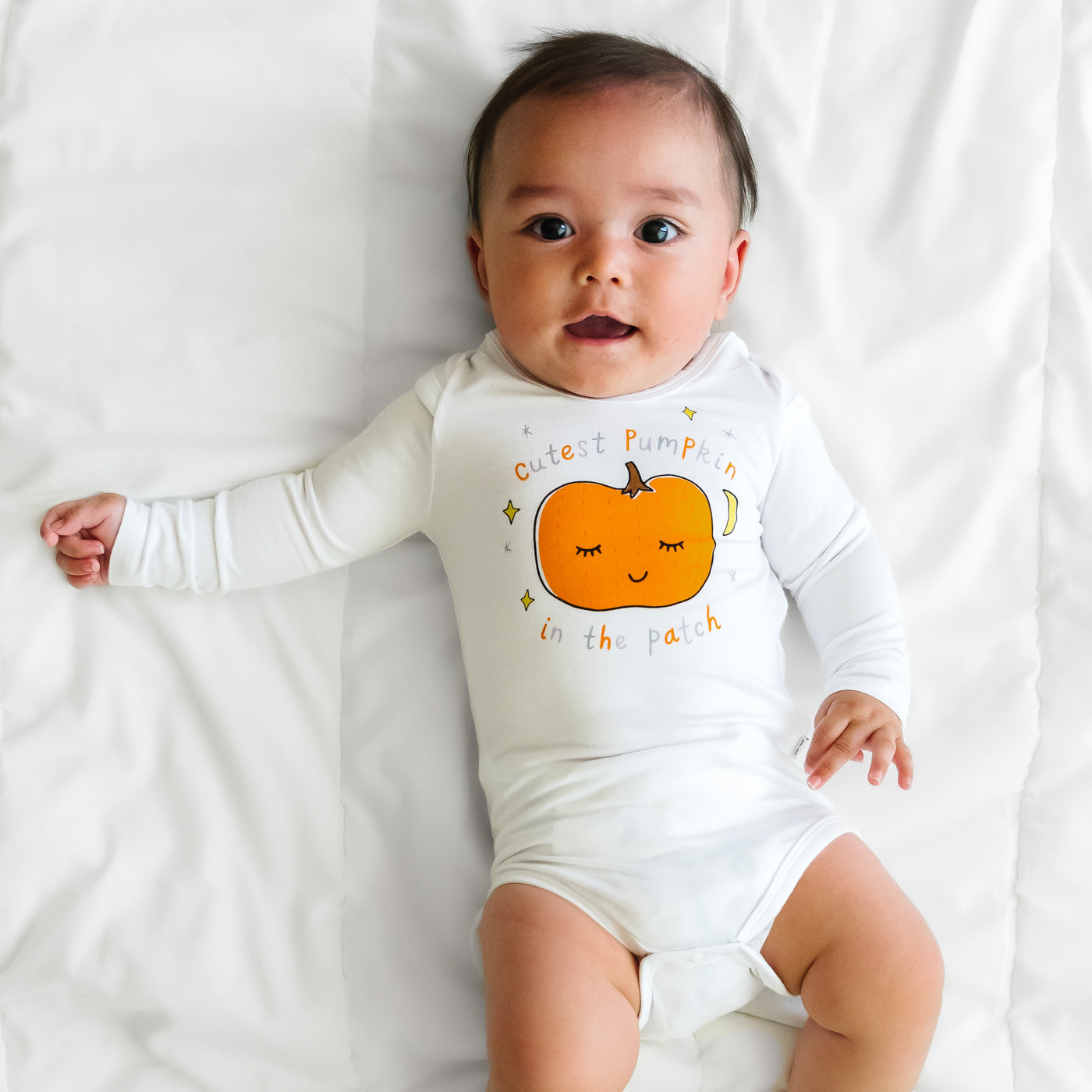 Child laying on a bed wearing a Little Pumpkin graphic bodysuit