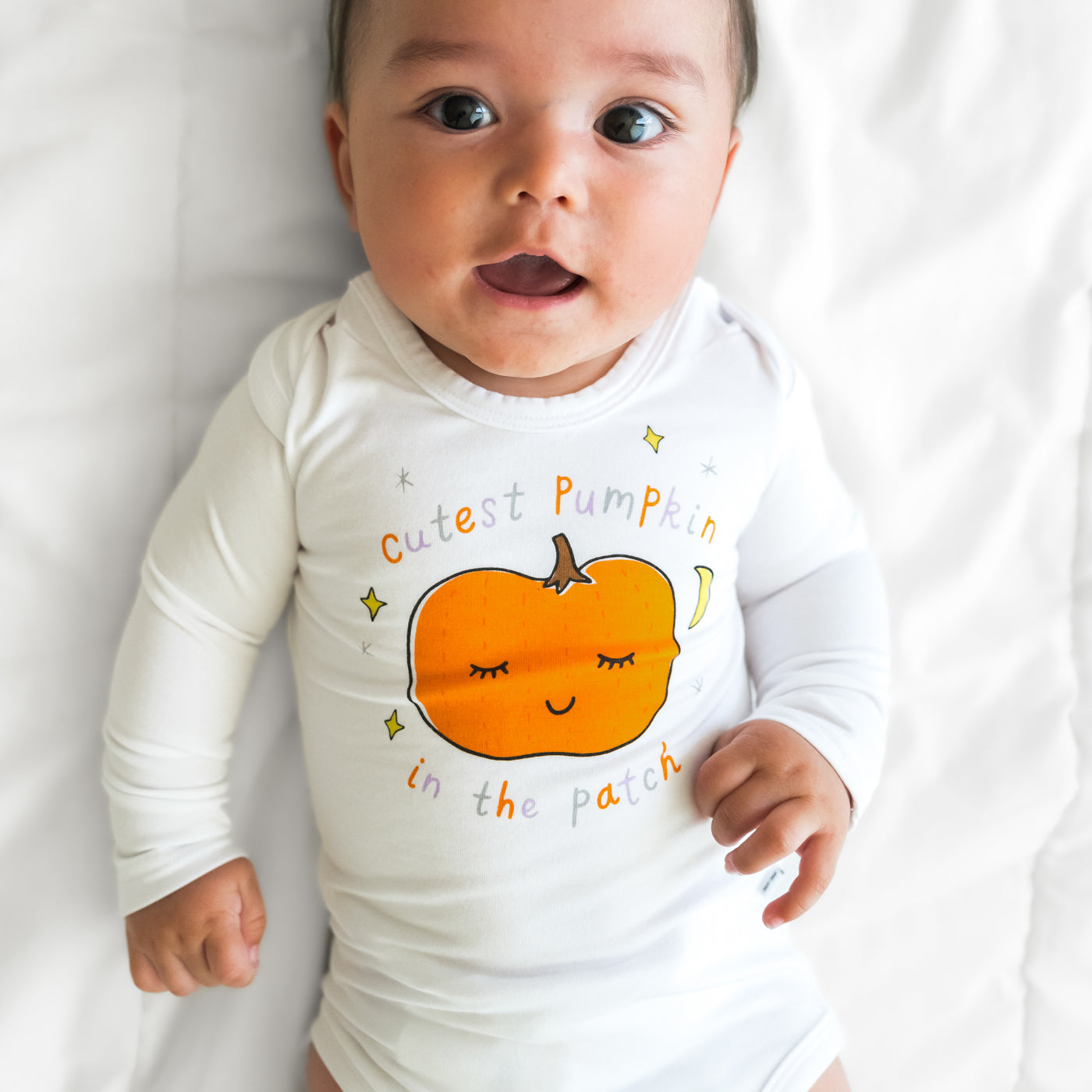 Close up image of a child laying on a bed wearing a Little Pumpkin graphic bodysuit