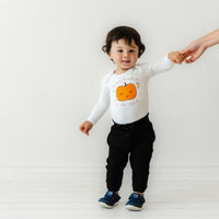 Child holding their mom's hand wearing a Little Pumpkin graphic bodysuit paired with Black Paperbag joggers