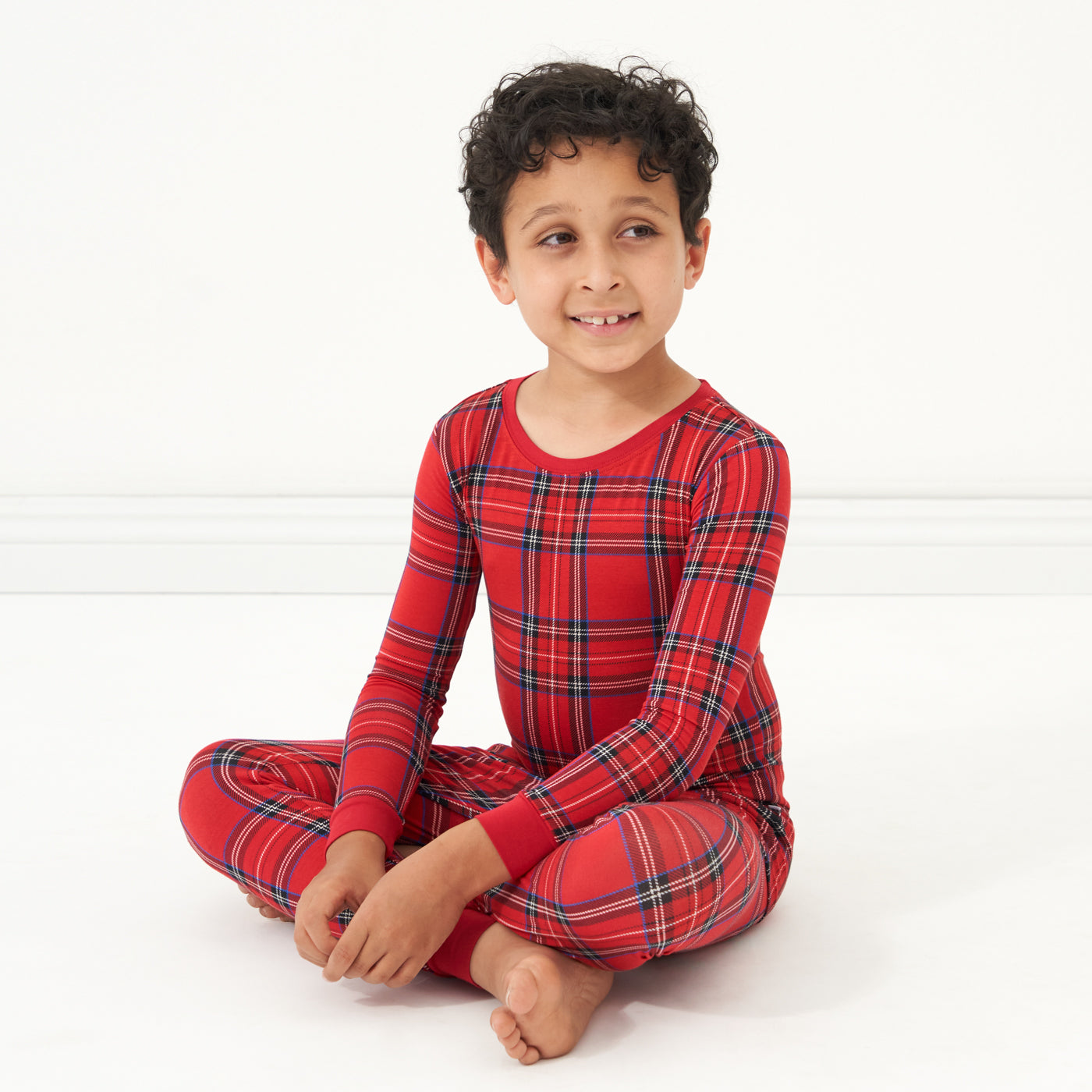 Child sitting on the ground wearing a Holiday Plaid two piece pajama set