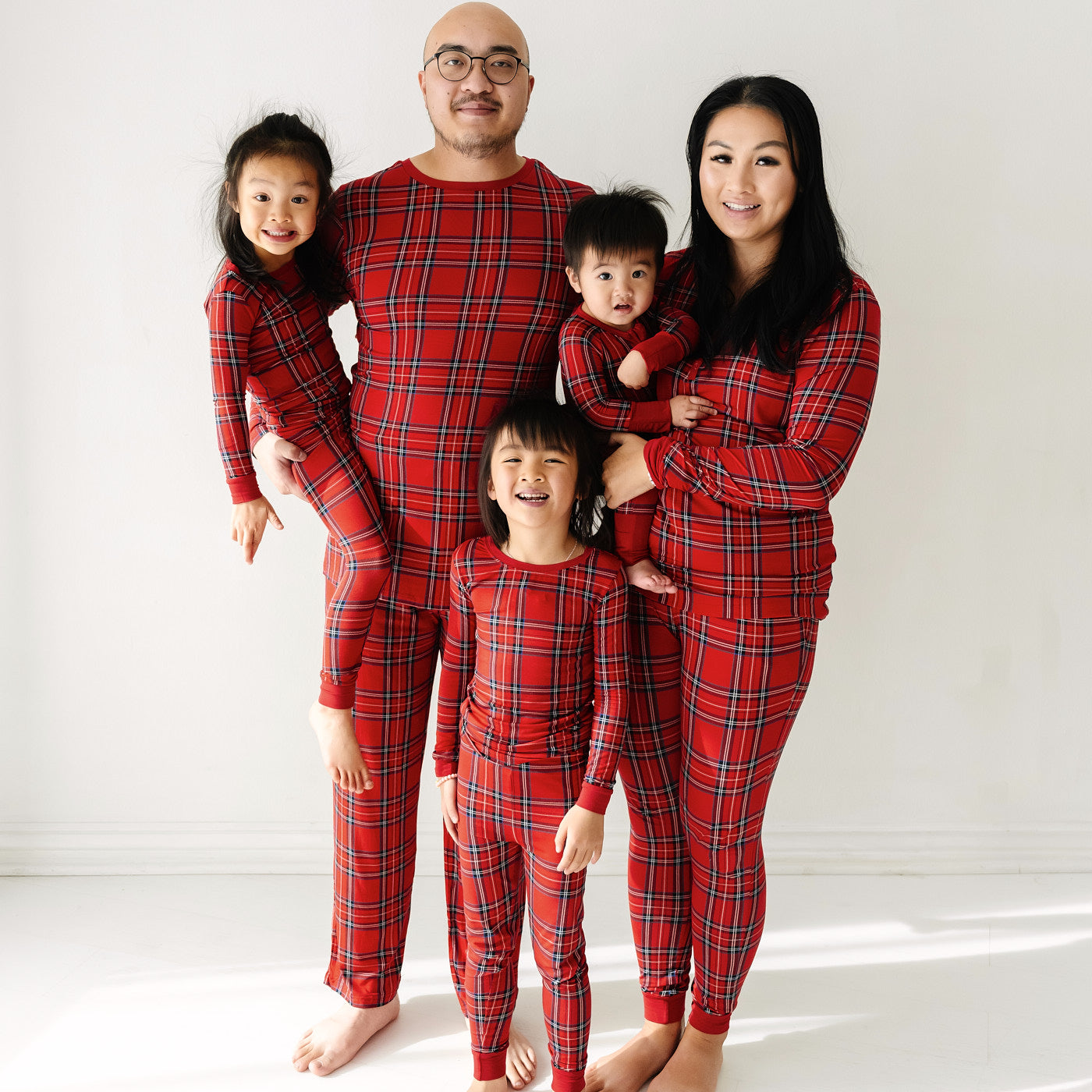 Family of five wearing matching Holiday Plaid pajamas in men's, women's, and children's two piece styles