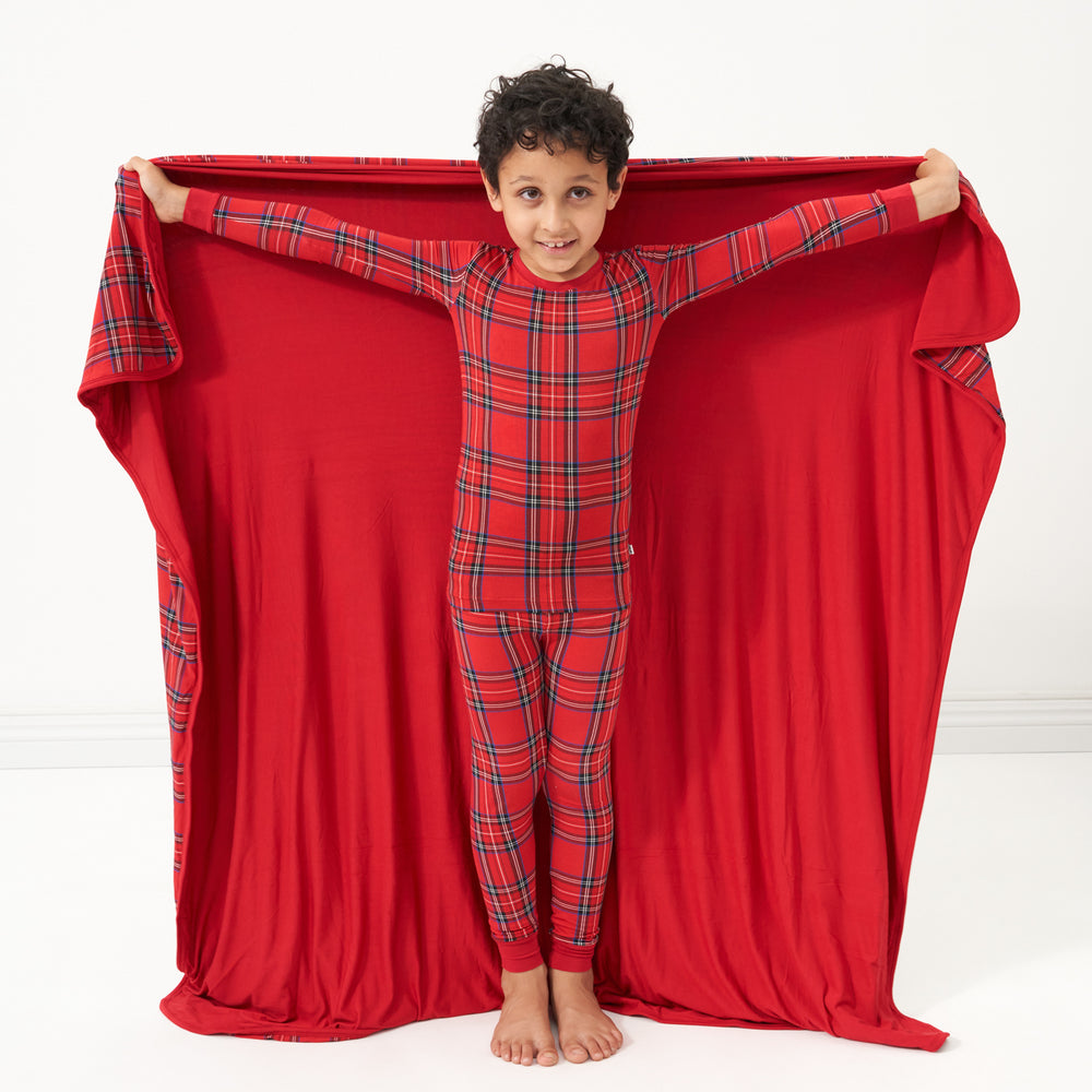Child holding out a Holiday Plaid large cloud blanket behind them showing the solid red backing