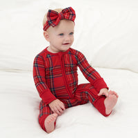 Child sitting on a bed wearing a Holiday Plaid luxe bow headband and matching zippy