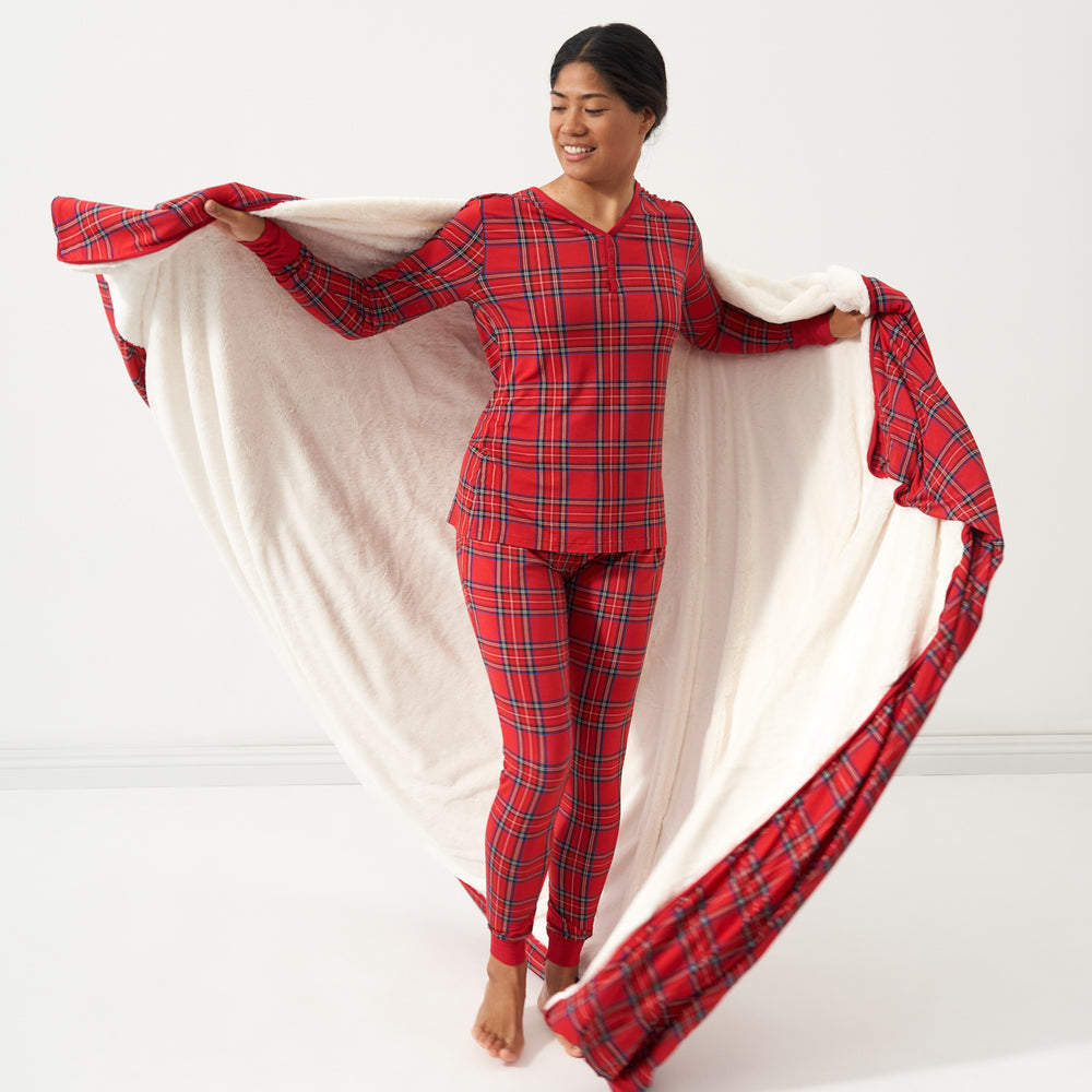 Woman holding a Holiday Plaid plush oversized cloud blanket out behind her showing the solid white backing