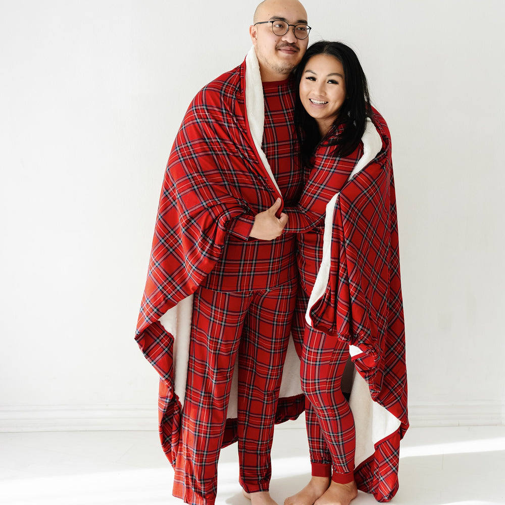 Man and woman snuggling under a Holiday Plaid overrsized plush blanket wearing matching men and women's Holiday Plaid pajama sets