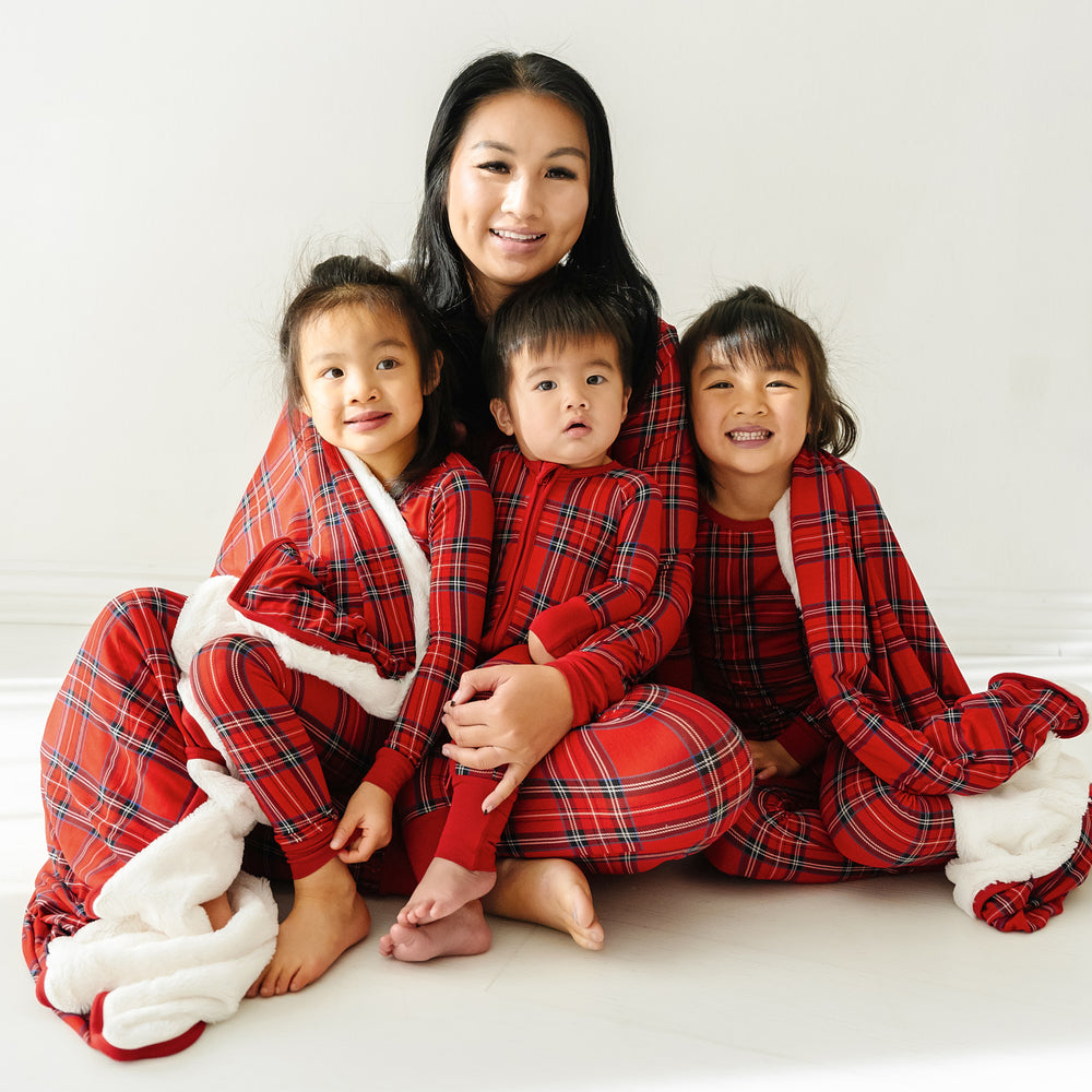 Mother and her three children cuddling under a Holiday Plaid plush oversized cloud blanket wearing matching Holiday Plaid pajamas in women's and children's zippy styles