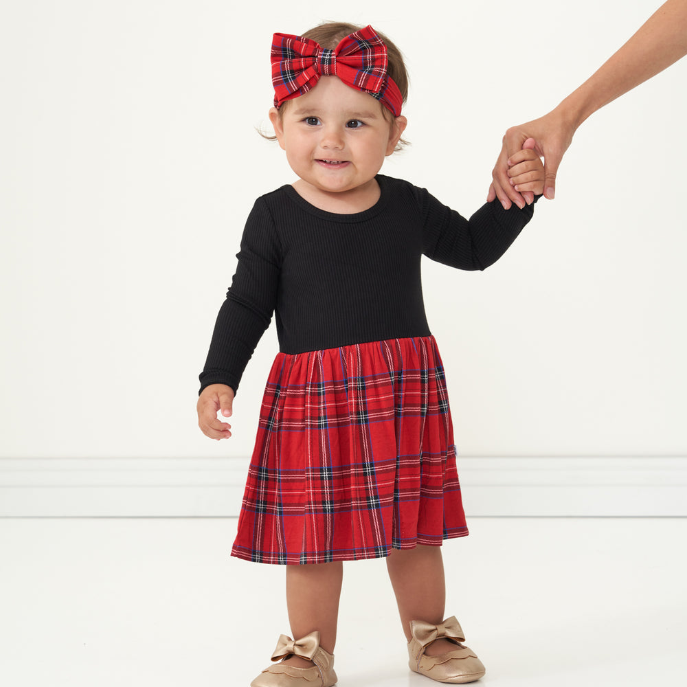 Child holding a parent's hand wearing a Holiday Plaid skater dress with bodysuit and matching luxe bow headband
