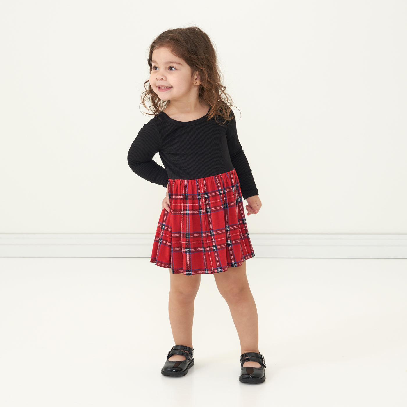 Child looking to the side wearing a Holiday Plaid skater dress with bodysuit