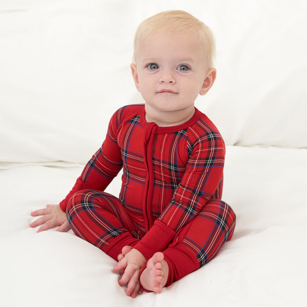 Child sitting on a bed wearing a Holiday Plaid zippy