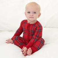 Child sitting on a bed wearing a Holiday Plaid zippy