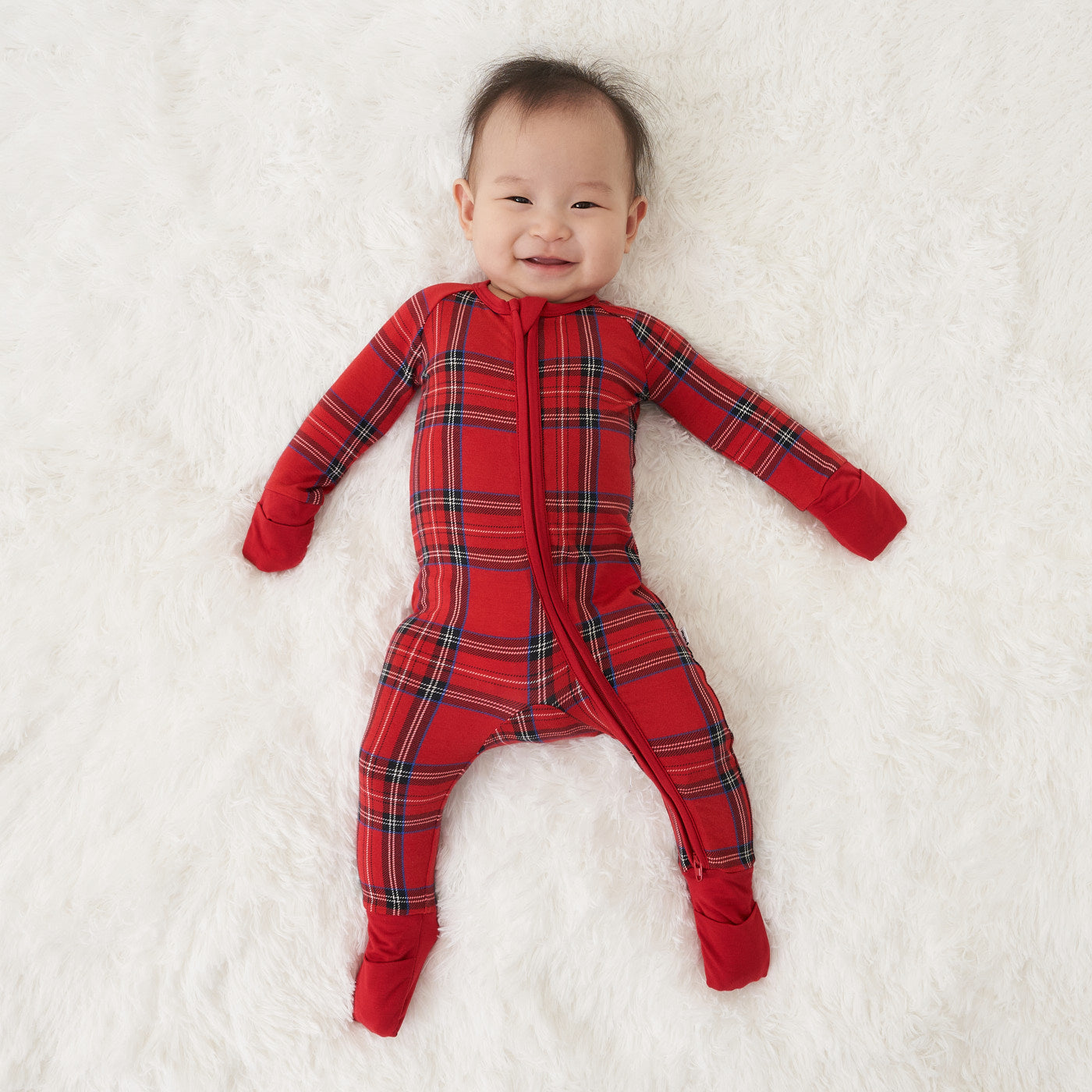 child laying on a blanket wearing a Holiday Plaid zippy showing off the fold over mittens and feet 