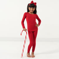 Child posing with a large candy cane wearing a Holiday Red two-piece pajama set