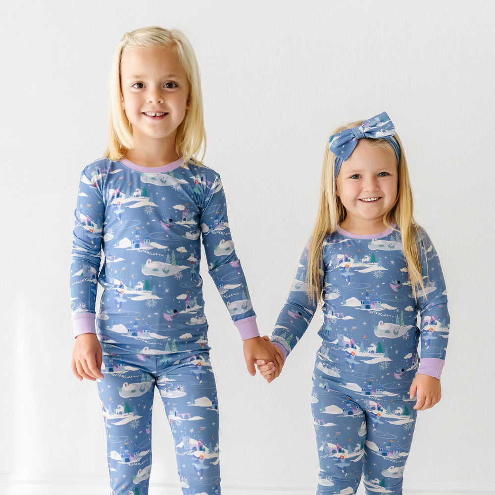 Two children holding hands wearing matching Ice Princess two piece pajama sets paired with a matching Ice Princess luxe bow headband
