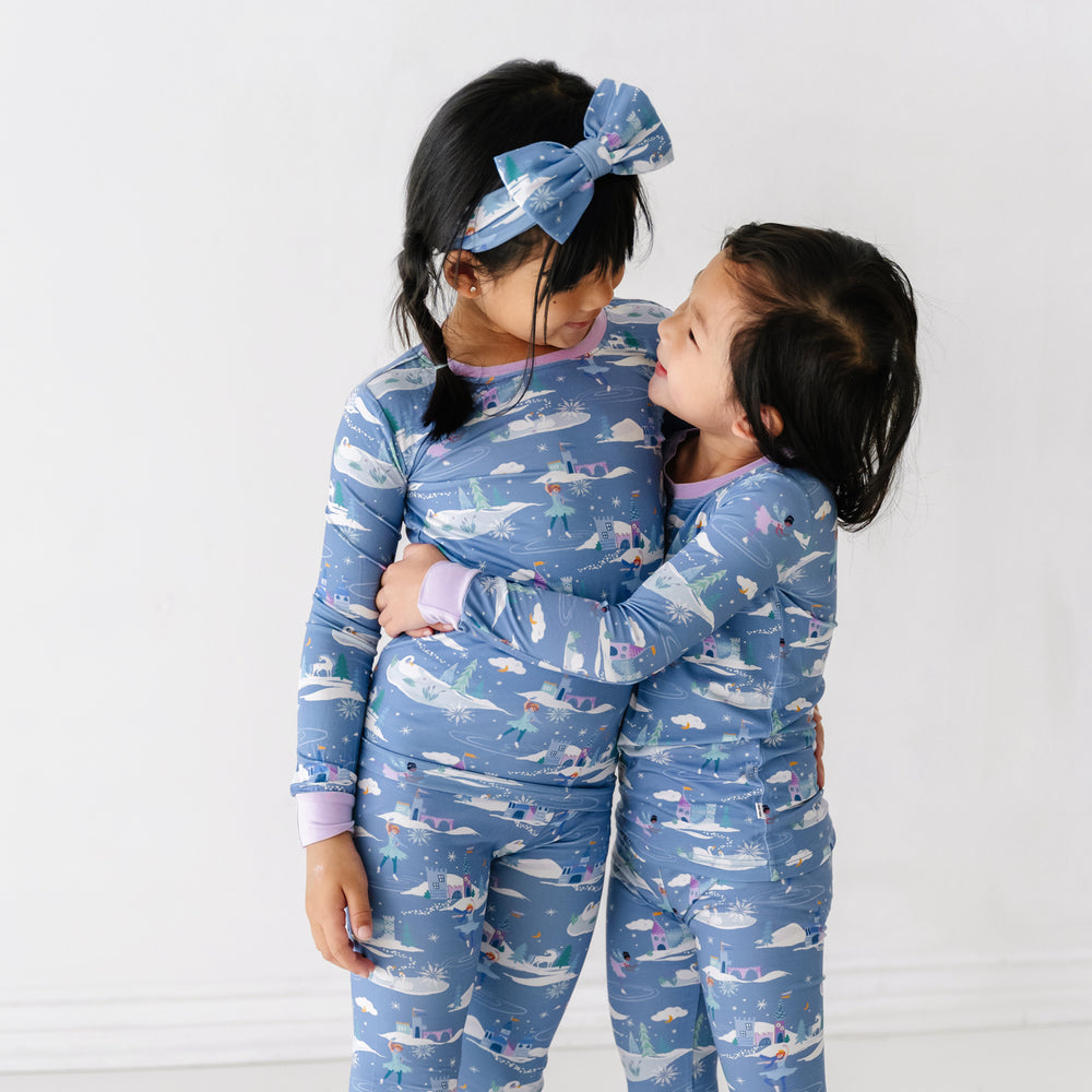 Two children hugging wearing matching Ice Princess two piece pajama sets paired with a matching Ice Princess luxe bow headband