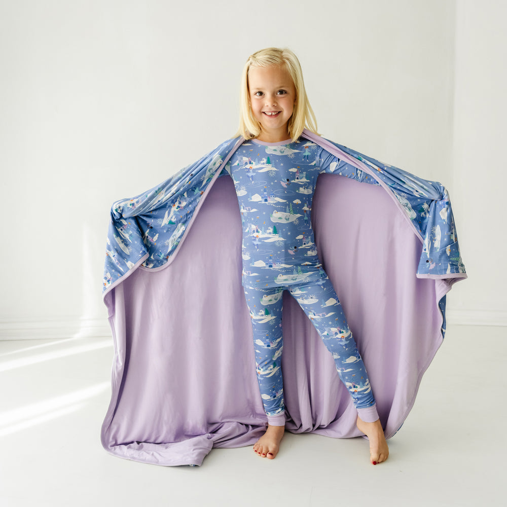 Child holding out an Ice Princess printed cloud blanket showing the solid purple backing. She is wearing matching Ice Princess printed two piece pajama set