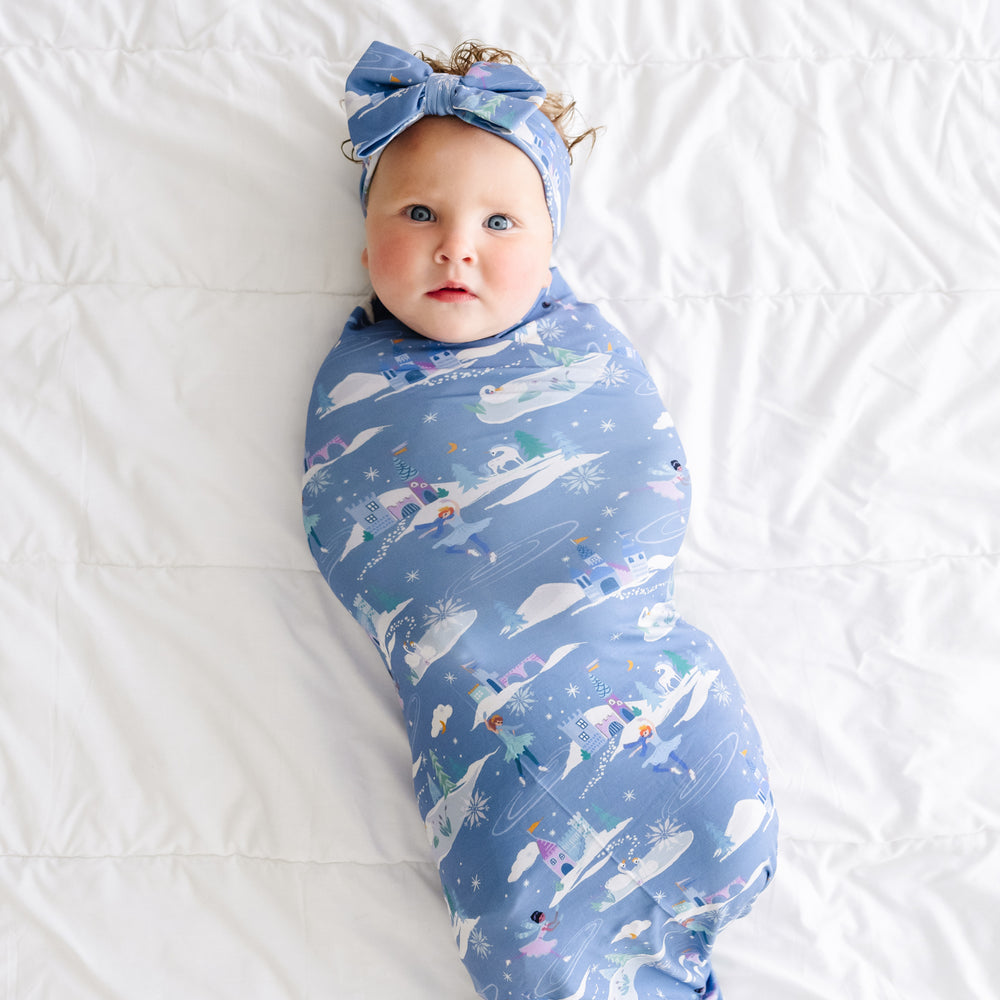 Child laying on a bed swaddled in an Ice Princess printed swaddle and luxe bow headband set