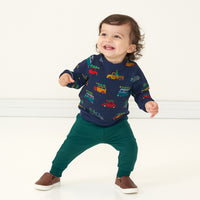 Child posing wearing Emerald Joggers paired with a Tree Traffic printed crewneck