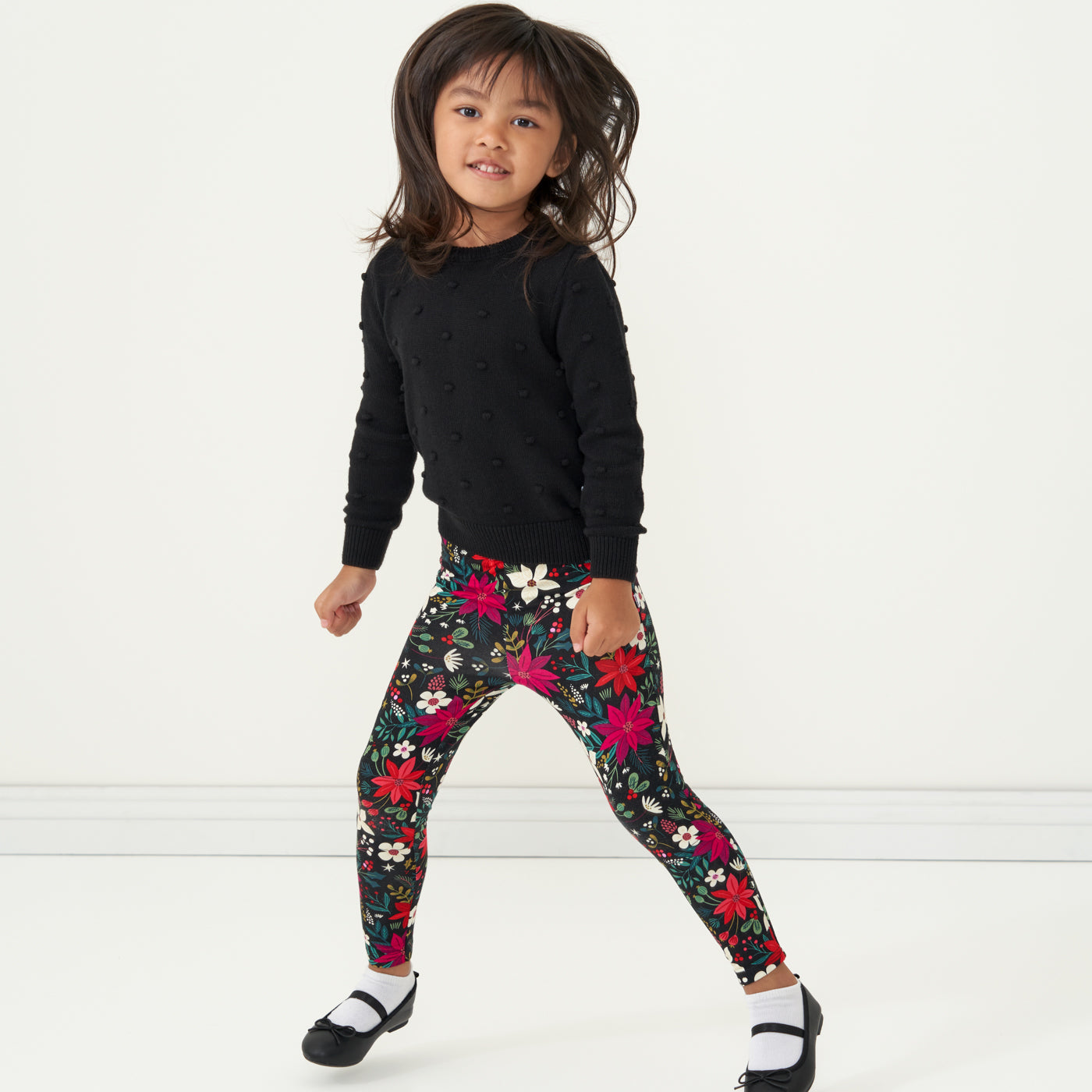 Child jumping wearing Berry Merry Leggings paired with a Black Pom Pom Sweater