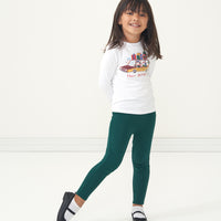 Child posing wearing Emerald leggings paired with a Happy Howlidays graphic tee