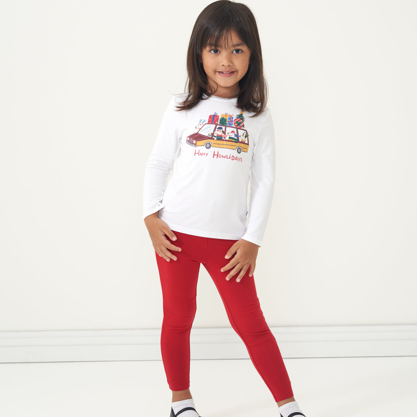 Child posing wearing Holiday Red leggings paired with a Happy Howlidays graphic tee