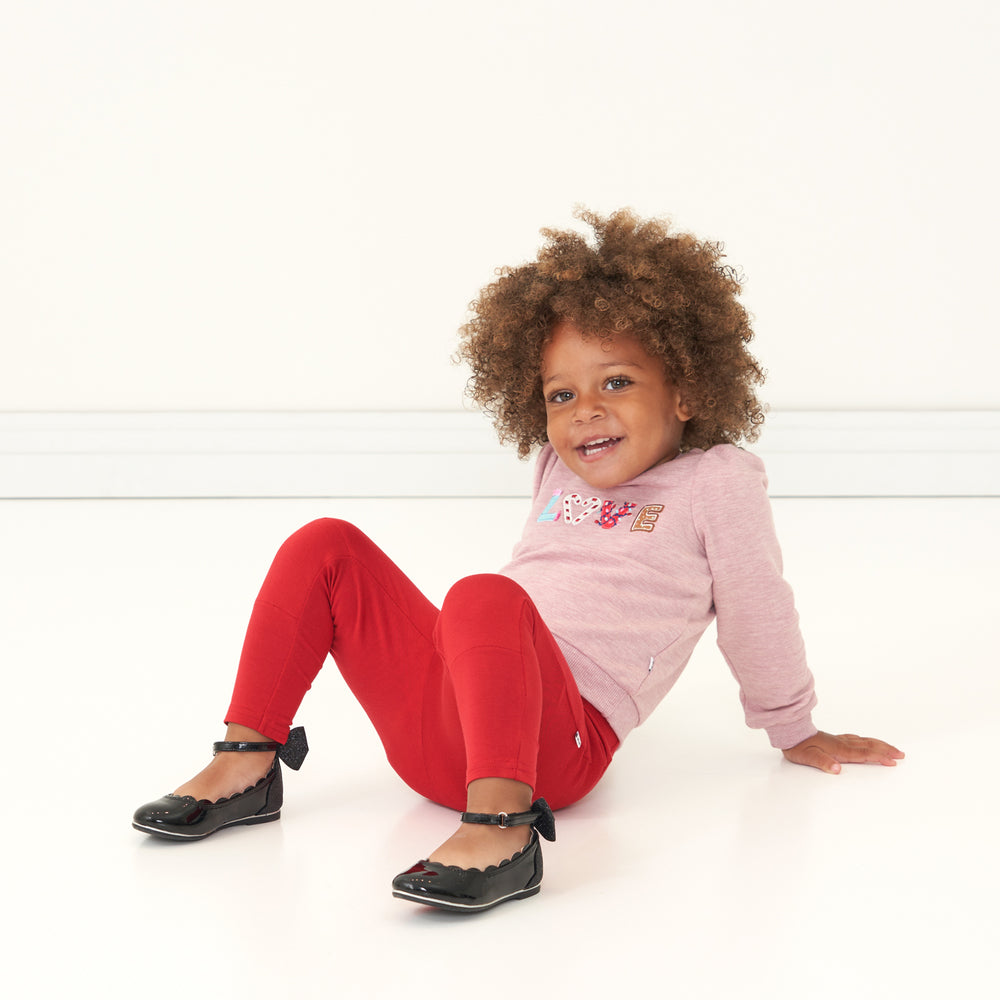 Child sitting wearing Holiday Red Leggings paired with a Heather Mauve Love Puff Sleeve Crewneck 