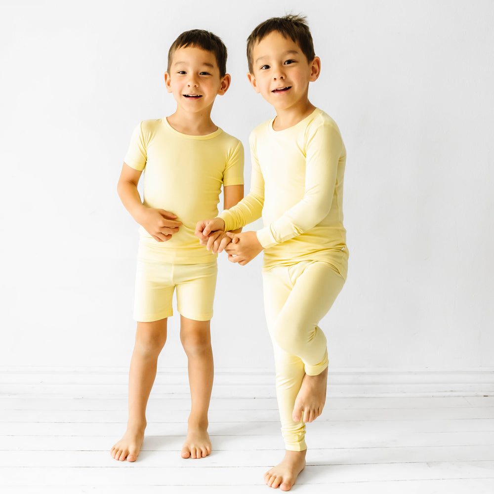 Two children holding hands wearing matching Lemon Twist pajama sets. One child is wearing a Lemon Twist two piece short sleeve and shorts pajama set. The other child is wearing a Lemon Twist two piece pajama set
