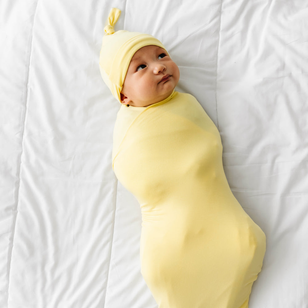 Child laying on a bed swaddled in a Lemon Twist swaddle and hat set