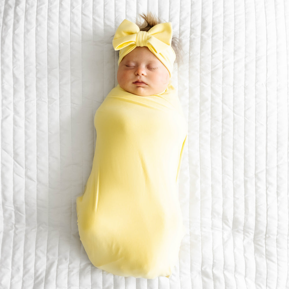 Child laying on a bed wearing a Lemon Twist swaddle and luxe bow headband set