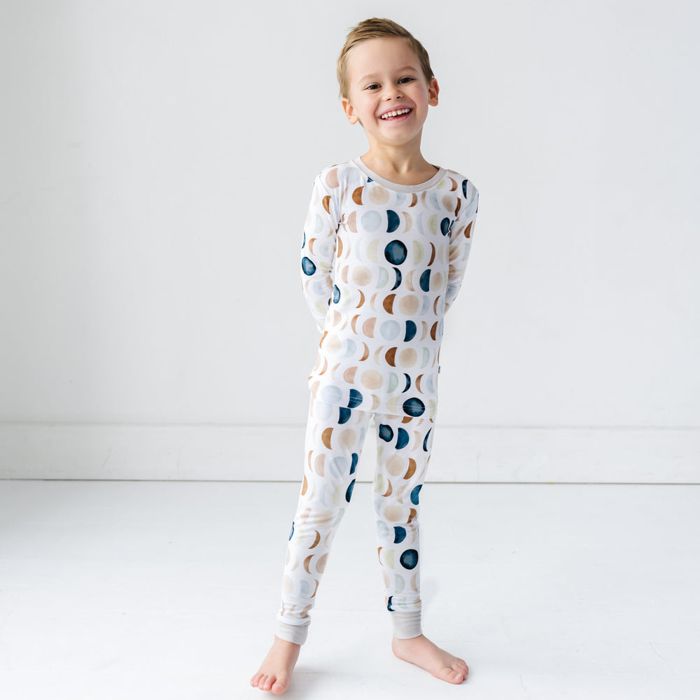 Click to see full screen - Image of a toddler in long sleeve top and pajama pants set in Luna Neutral print. This print features phases of the moon in the sweetest shades of creams, tans, and navy watercolor in an all over repeat pattern.