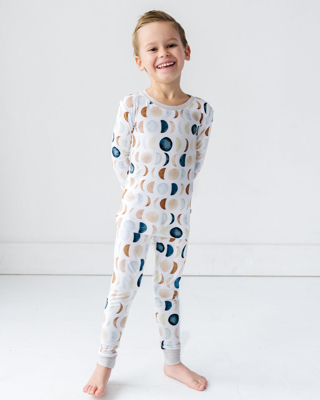 Image of a toddler in long sleeve top and pajama pants set in Luna Neutral print. This print features phases of the moon in the sweetest shades of creams, tans, and navy watercolor in an all over repeat pattern.