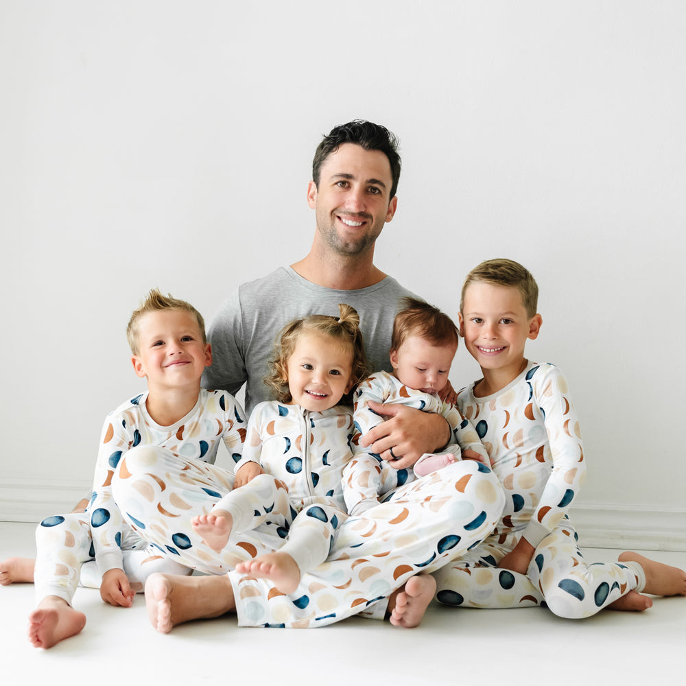 Father and his four children wearing coordinating Luna Neutral pajamas. Dad is wearing men's Heather Gray pajama top paired with men's Luna Neutral pj pants. His children are wearing Luna Neutral pjs in two piece and zippy styles.