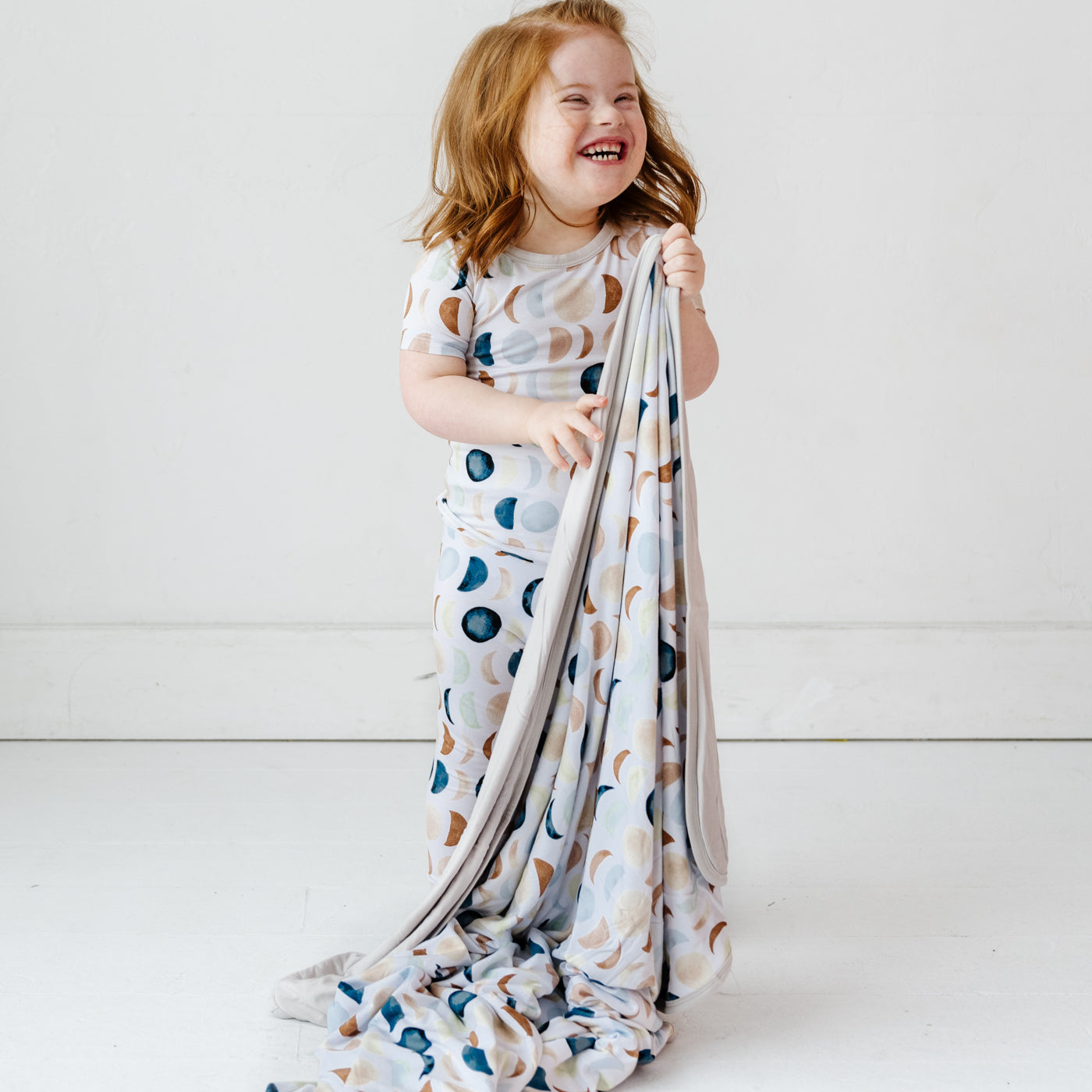 Child wearing a Luna Neutral two piece short sleeve pj set holding a Luna Neutral large cloud blanket