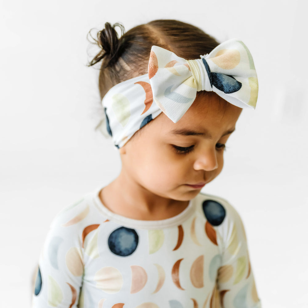 Click to see full screen - alternate profile image of a child wearing a Luna Neutral luxe bow headband paired with a matching two piece pajama set