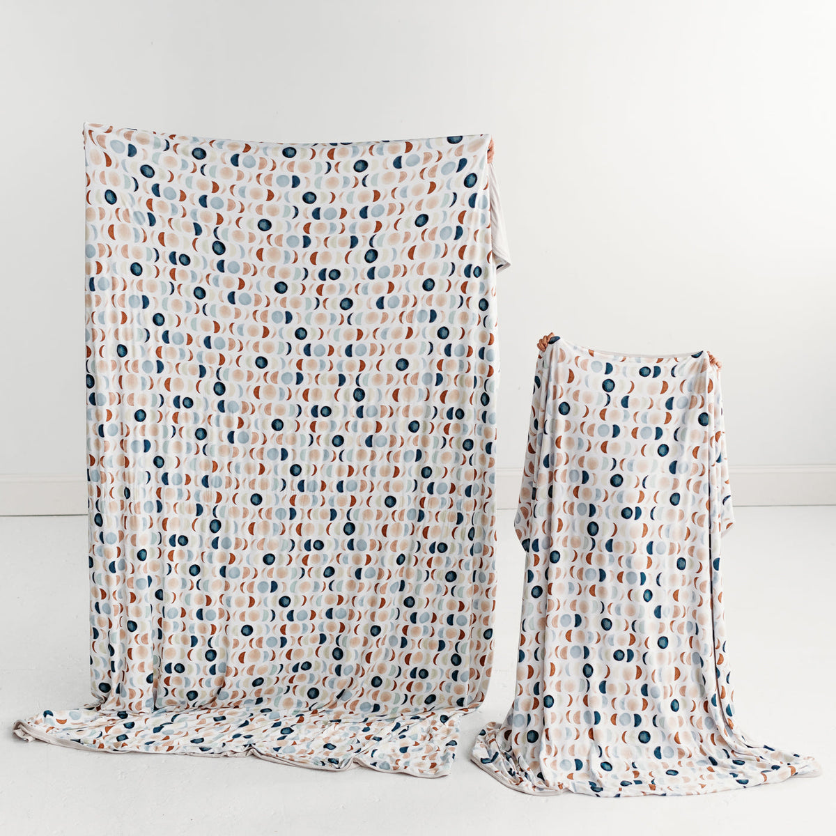Mother and child holding up matching Luna Neutral bamboo blankets. Mom is holding up an oversized bamboo blanket and child is holding up a large bamboo blanket.