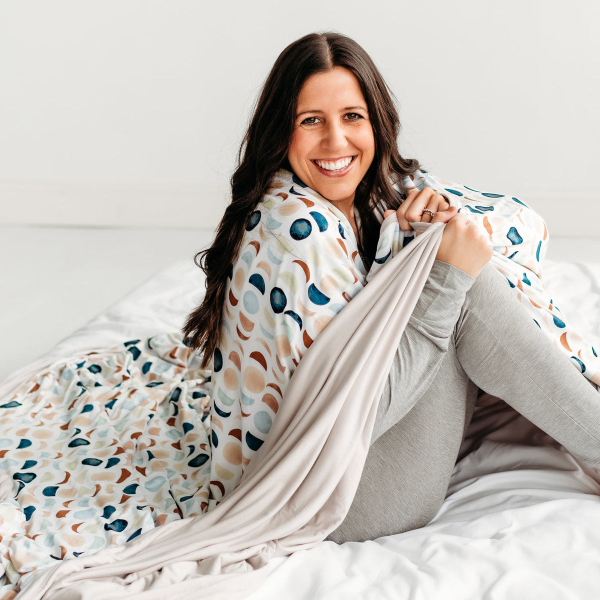 Woman sitting on the floor, wrapped up in a Luna Neutral oversized bamboo blanket.