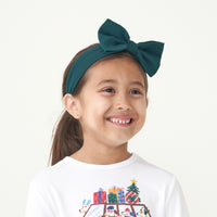 Child wearing a Happy Howlidays graphic tee paired with an Emerald luxe bow headband
