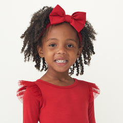 Child wearing a Holiday Red flutter tutu dress paired with a matching Holiday Red luxe bow headband